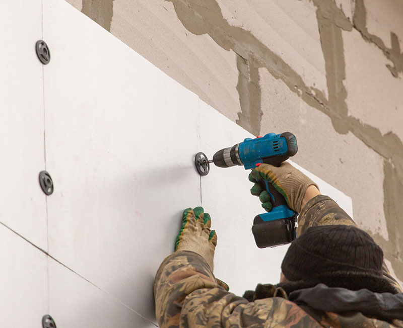 Ouvrier appliquant des plaques isolantes sur les murs d'une maison